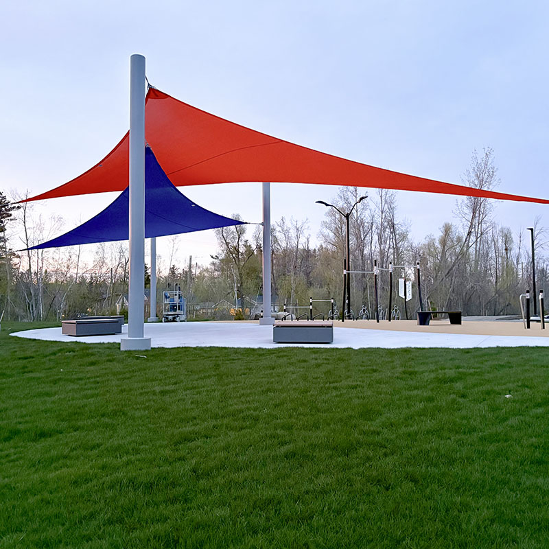 A ground-level view of a commercial-grade multiple post shade installation in a public park, featuring durable orange and blue fabric sails that overlap to create architectural interest and maximum UV protection.