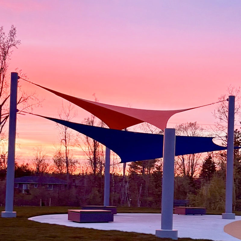A scenic shot of a Sun Shade Co. multiple post shade system, showcasing the clean lines of the grey support columns and the sleek, tensioned design of the orange and blue triangular sails.
