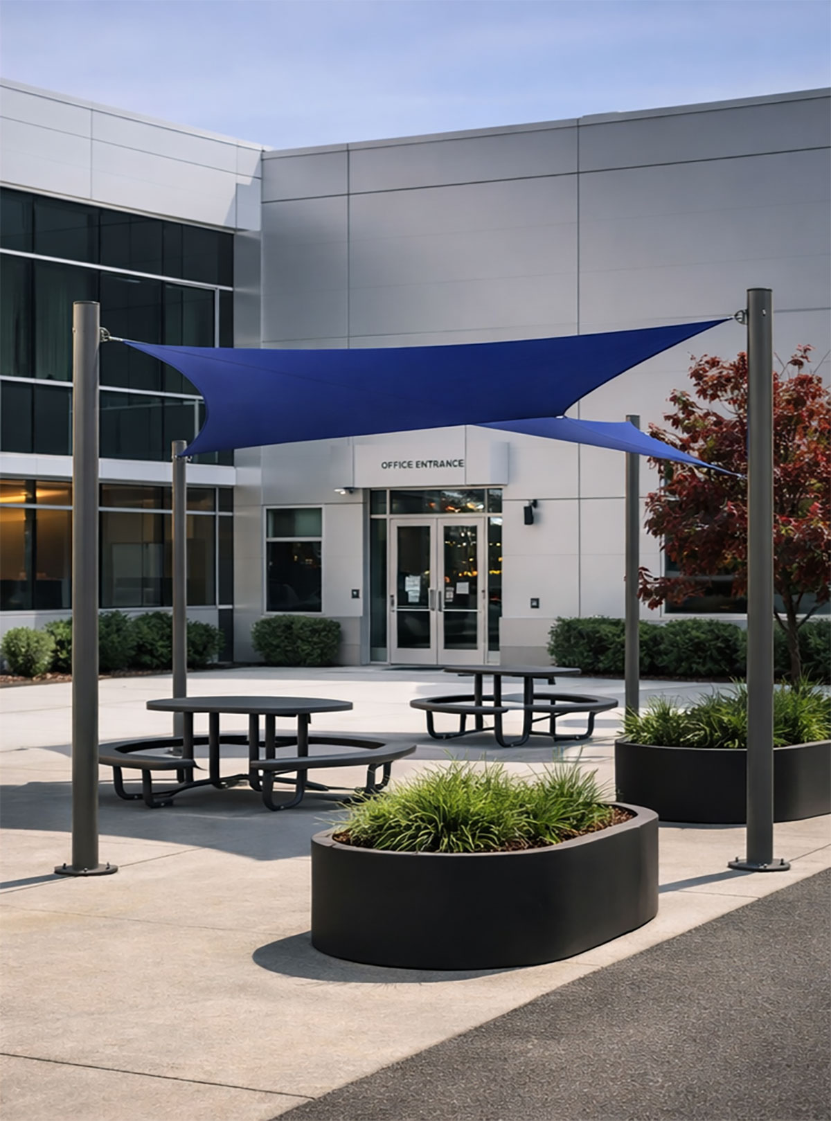 Aquatic blue 4-Post Super Shade structure installed over circular outdoor seating and planters at a modern commercial office entrance.