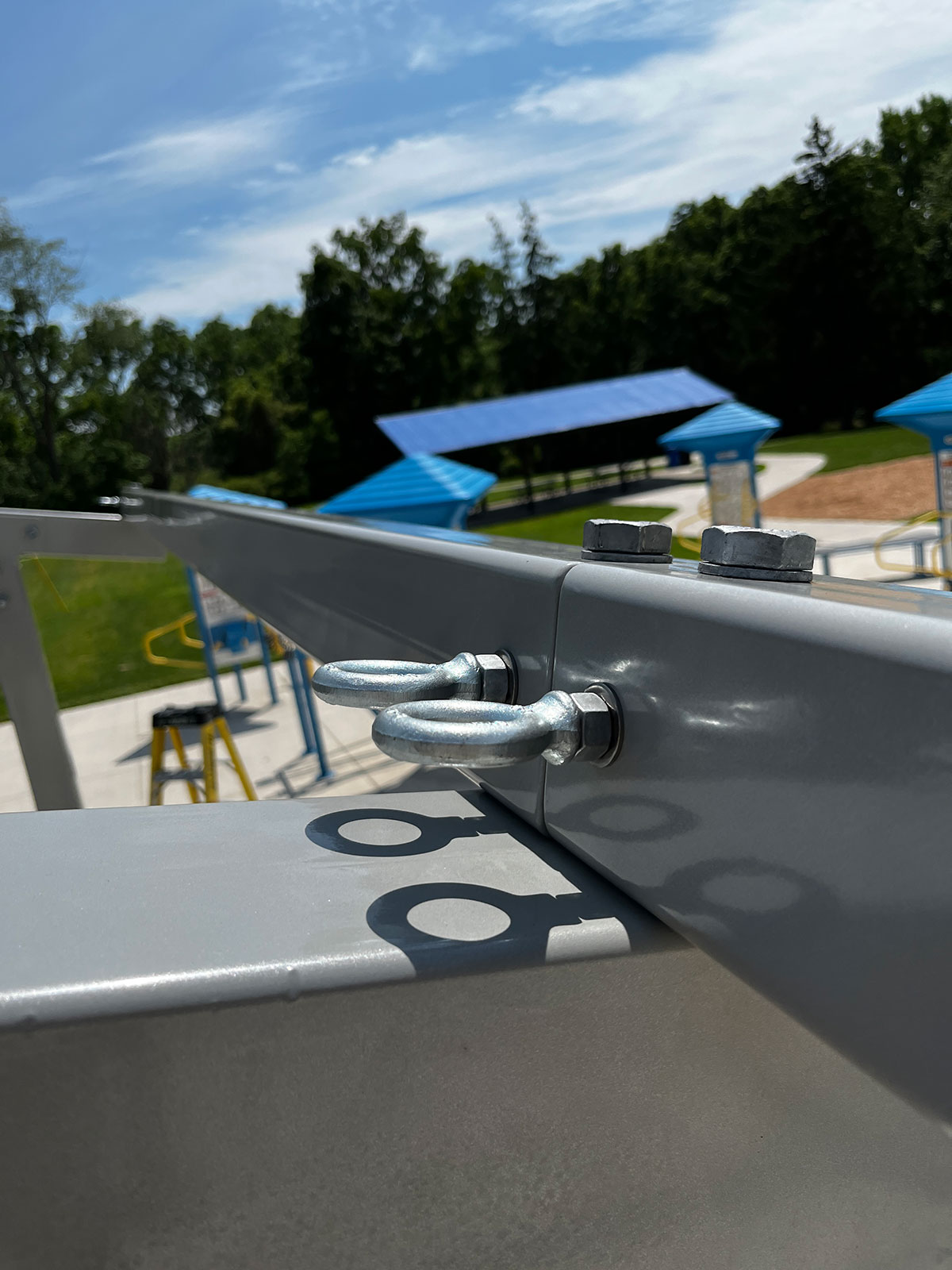 Close-up of heavy-duty steel eye bolts installed on a gray metal support frame for an outdoor patio shade structure.