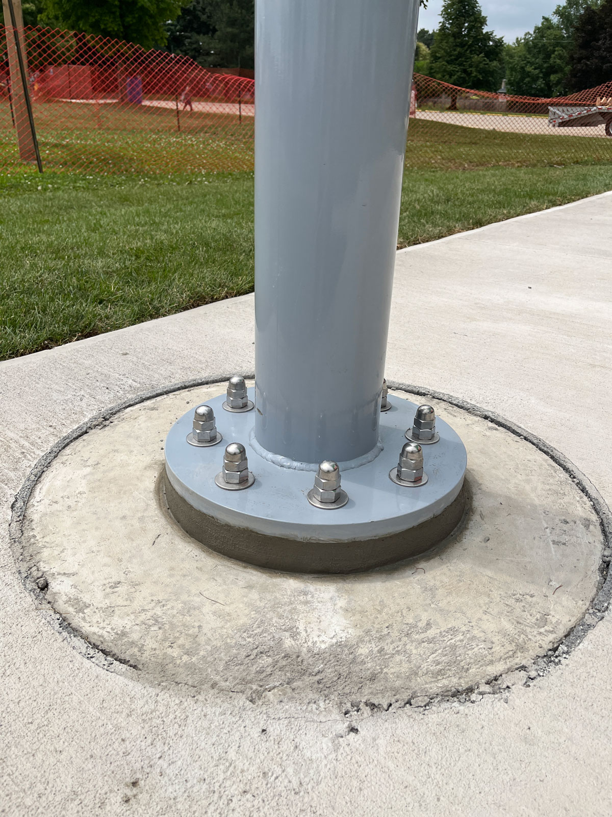 A gray powder-coated steel shade sail pole securely bolted with concrete anchor fasteners into a round cement foundation base.