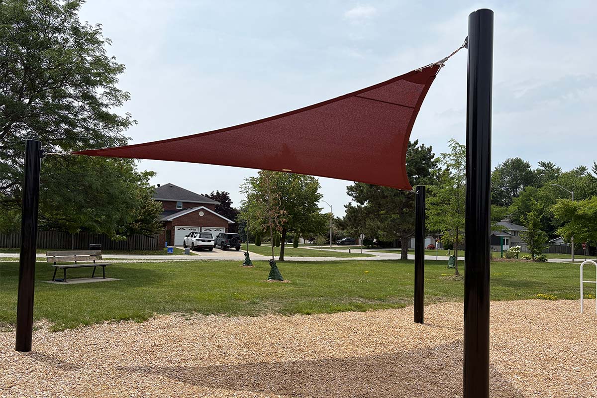 Red triangle shade sail providing sun protection over a community playground.