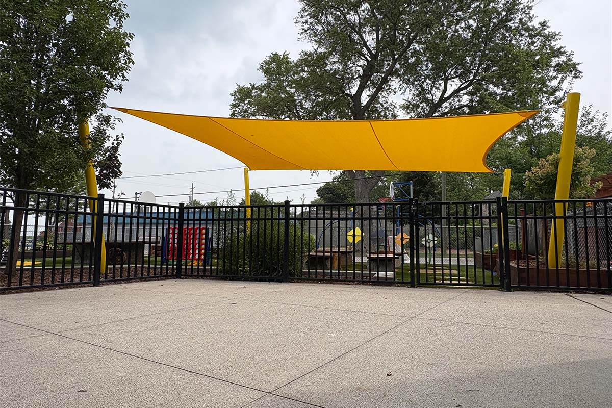Yellow 4 post playground shade sail providing outdoor sun protection at a childcare play area.