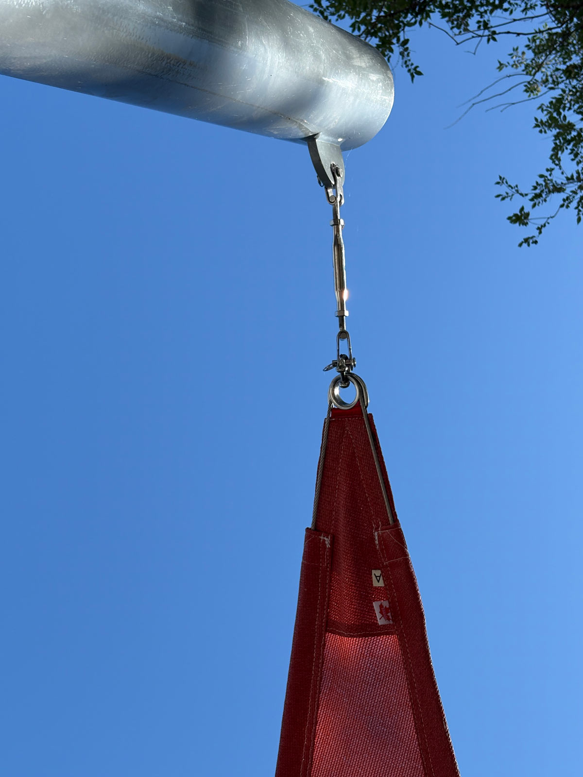 Shade sail tensioning hardware, turnbuckle, and anchor attachment point connected to a metal support post.