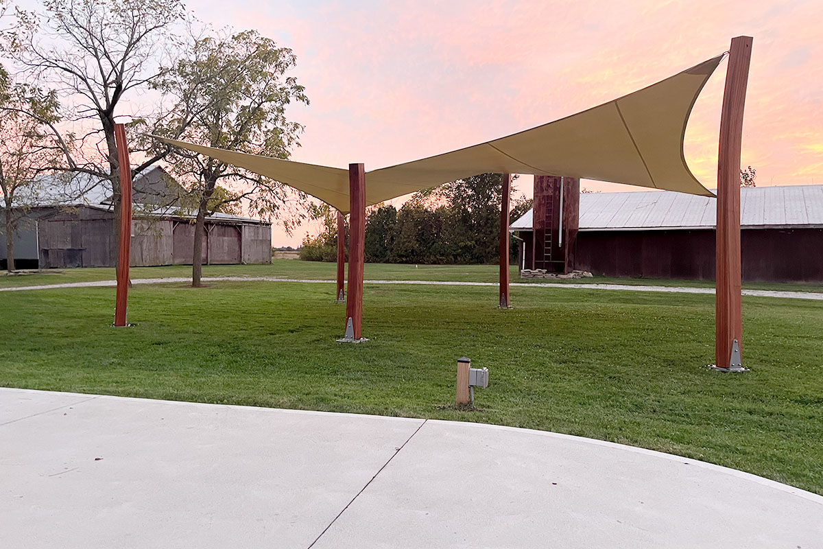 Professional shade sail installation featuring a sloped design mounted on sturdy wooden posts in a park.