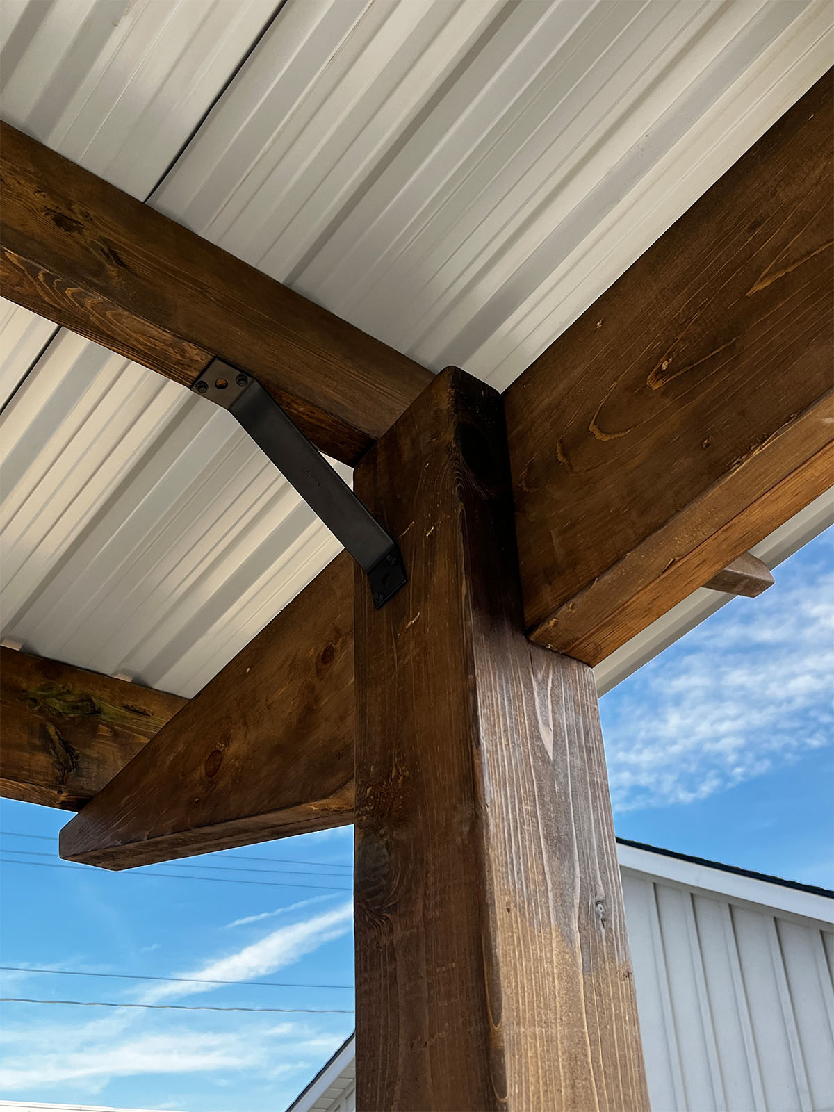 A close-up view of heavy-duty black metal corner brackets securing wooden beams under a solid white architectural steel shade.