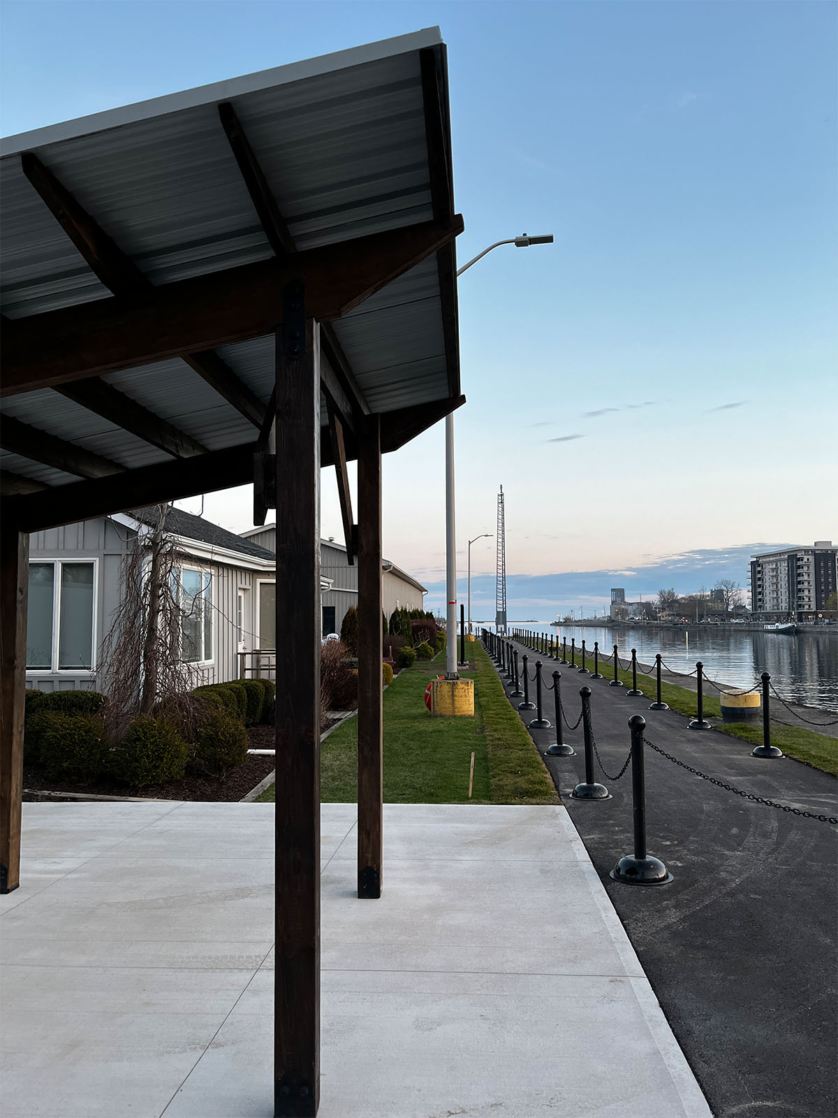 A custom architectural steel shade structure installed along a scenic waterfront pathway next to a concrete walkway and marina.